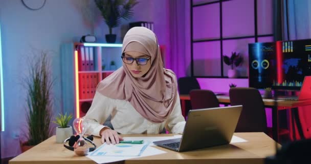 Επιχειρηματική έννοια όπου όμορφη αυτοπεποίθηση έμπειρη αραβική επιχειρηματίας σε hijab ανάγνωση πληροφοριών στις εκθέσεις και την εισαγωγή δεδομένων σε φορητό υπολογιστή στο γραφείο το βράδυ — Αρχείο Βίντεο