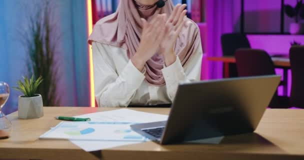 Aantrekkelijke tevreden succesvolle ervaren Arabische zakenvrouw in hijab draagt headset tijdens online chatten op laptop met collega 's en klappen handen na effectief gesprek — Stockvideo