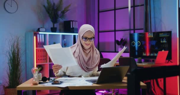 Krásná přešťastný úspěšný arabský podnikatel v hidžábu čtení dobré zprávy na obrazovce notebooku a rozptýlení papíry přes hlavu ve večerní kanceláři, úspěch a štěstí koncept — Stock video