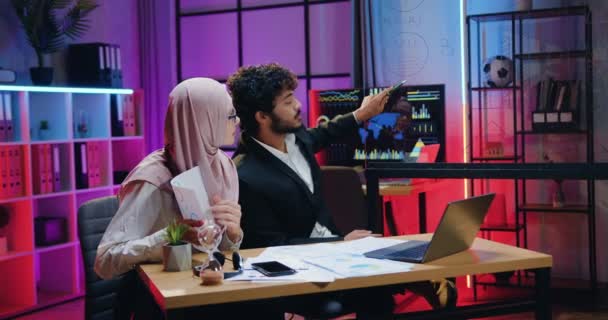 Attrayant confiant bonne humeur responsable musulman hommes et femmes collègues d'affaires tenant une vidéoconférence avec des partenaires d'affaires sur ordinateur dans le bureau du soir — Video