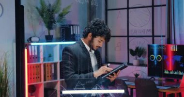 Çekici, konsantre, maksatlı, Müslüman, sakallı, işgüzar adam tablet bilgisayardaki bilgileri kontrol ediyor ve akşam çalışma odasındaki cam verilerle karşılaştırıyor.