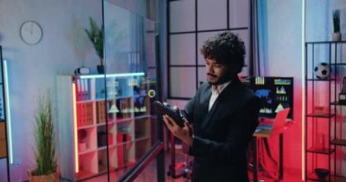 Çekici, konsantre, yüksek motivasyona sahip, takım elbiseli, sakallı, Müslüman ofis çalışanı gece mesaisinde çalışırken tablet bilgisayarın cam duvarına notlar yazması gerekiyordu.