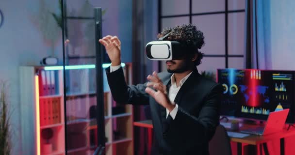 Concept de technologie moderne où l'homme barbu intelligent concentré attrayant habillé en costume portant des lunettes de réalité augmentée travaillant sur écran imaginaire dans la salle de travail du soir — Video