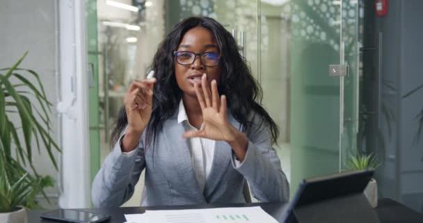Charming confident successful modern black-skinned female office worker talking on camera while holding online video conference and explaining infographics with flowcharts — Stockvideo