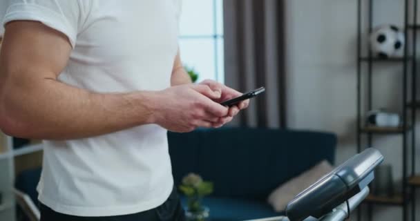 Desconocido fuerte chico deportivo activo utiliza su teléfono durante el entrenamiento en casa por la mañana en pista de atletismo, concepto de estilo de vida saludable — Vídeos de Stock