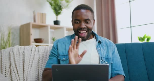 Attraente gioioso felice spensierato giovane barbuto africano americano ha video chat con un amico o un parente sul computer portatile e agitando la mano per dire addio quando si conclude la conversazione — Video Stock