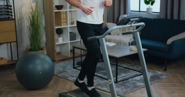 Концепція домашнього тренування, де приємно впевнений спортивний молодий бородатий чоловік у спортивному одязі бігає на біговій доріжці вранці або вдень — стокове відео