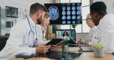 Çekici, kendine güvenen, çalışkan, çok ırklı doktorlardan oluşan bir ekip, dizüstü bilgisayarlı, Afrikalı Amerikalı kadın başhekimle online istişare sırasında klinikteki masada oturuyor.
