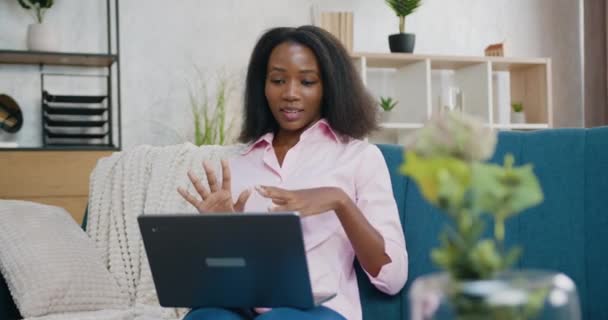 Dość zadowolony pozytywne beztroskie młoda Afroamerykanka kobieta siedzi na kanapie przed komputerem podczas czatu wideo online z przyjacielem lub krewnym w domu — Wideo stockowe