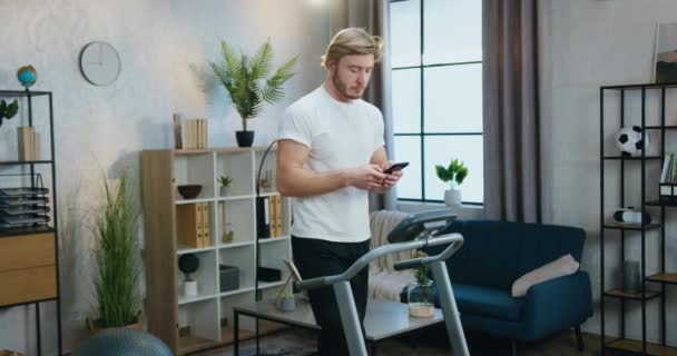 건강 한 생활 방식이라는 개념은 운동복을 입은 남성 이 러닝 머신에서 집안일을 하고 스마트폰을 사용하여 친구들 과대화하는 것이다 — 비디오