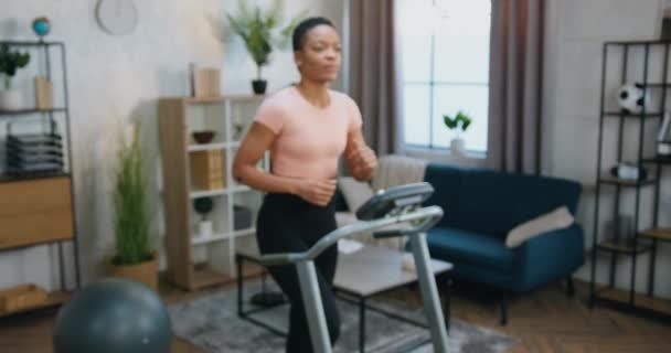 Câmera de tiro em bonito satisfeito esportivo magro afro-americano mulher em roupas de treinamento que fazendo exercícios de caminhada na pista de corrida em casa — Vídeo de Stock