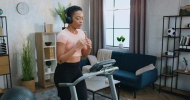 Koşu bandında koşan ve kulaklıkla favori müziği dinleyen sevimli, gülümseyen Afro-Amerikan kadın.