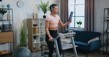 Eğitimli, aktif, zayıf ve sportif bir iş kadını, koşu bandında koşu bandında antrenman yaparken, tablet cihazında video çağrısı yaparken kulaklık takıyor.