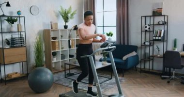 Spor giyimli, spor giyinen, su içen ve çalışan bir makinede yürürken vücut suyunu yeniden düzenleyen oldukça yorgun genç bir kadının olduğu ev yapımı egzersiz konsepti.