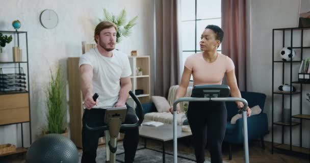 스 포오 츠 계의 매력적 인 활동적 인 다양 한 부부가 러닝 머신 과 자전거 조련사와 함께 운동을 하는 가정 운동 개념 — 비디오