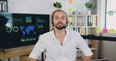 Kafkasyalı başarılı adam portresi kulaklıklı çağrı merkezi ajanı modern ofiste online eğitim webinarı yönetiyor.