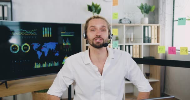 Retrato de feliz caucasiano agente de centro de chamadas de homem bem sucedido em headset realiza webinar de treinamento on-line no escritório moderno — Vídeo de Stock