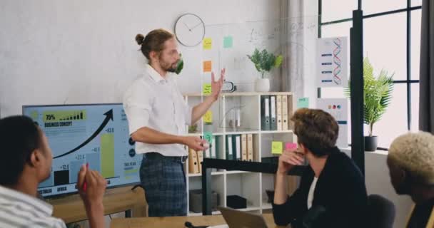 Ansehnlicher junger männlicher Manager, der während eines kreativen Brainstormings modernes Büro-Meeting mit Glasscheibe und digitalem Whiteboard vor seinen Kollegen präsentiert — Stockvideo