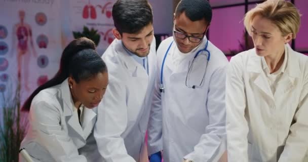Belle équipe d'hommes et de femmes médecins chimistes en blouse de laboratoire et gants stériles discutant des rapports médicaux et comparant les données avec l'information informatique — Video