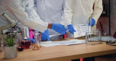 Tıbbi üniformalı ve steril eldivenli bilinmeyen bir doktor ekibi sağlık ofisinde masanın yanında duruyor ve raporda elde edilen sonuçları tartışıyorlar.