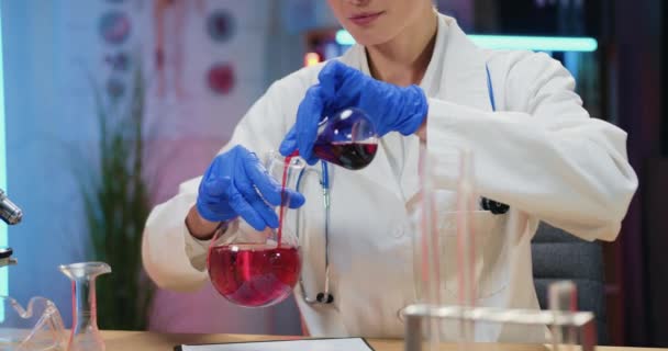 Attrayant concentré brillant qualifié femme blonde scientifique en blouse blanche et gants de protection mener des expériences chimiques avec des solutions dans des flacons dans le laboratoire du soir — Video