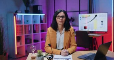 İş adamları konsepti, şık giyinen ve akşam ofisinde kameraya poz veren güzel, kendine güvenen, yüksek yetenekli esmer kadın.