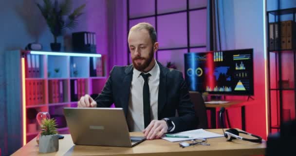 Beau concentré industrieux responsable habile homme d'affaires barbu assis sur son lieu de travail dans le bureau du soir et travaillant sur ordinateur — Video