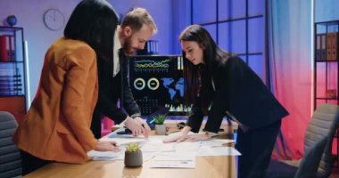 Ofisteki ortak proje üzerine yapılan beyin fırtınası sırasında masa başında duran ve kağıt raporlarını inceleyen kendinden emin, nitelikli kadın ve erkek ofis çalışanları.