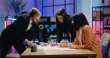 Çekici amaç güdümlü nitelikli erkek ve kadın ofis yöneticileri aktif olarak ortak iş projesini tartışıyorlar akşam ofislerinde masaya saçılmış kağıt raporları kullanarak.