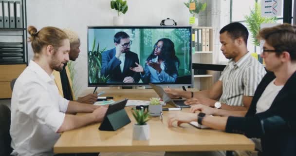 Kreatives Geschäftsteam applaudiert und gratuliert zwei jungen Geschäftsleuten, die mit Spannung vom Computerbildschirm aus über einen neuen erfolgreichen Vertrag sprechen, während sie sich online treffen — Stockvideo