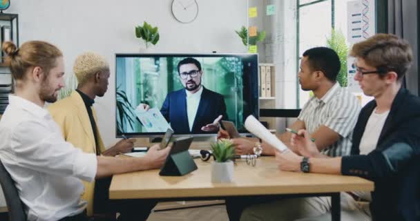 Diverso grupo masculino de gente de negocios que tiene videollamada de conferencia de negocios en línea en el monitor de pantalla de televisión en la sala de reuniones a bordo — Vídeos de Stock