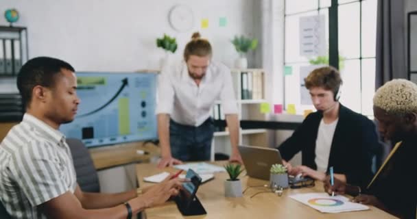 Retrato del exitoso líder de negocios masculino millennial en la oficina moderna, mirando a la cámara. Equipo diverso ocupado trabajando en segundo plano — Vídeos de Stock