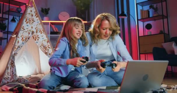Adorable cheerful happy playful adult mom and her teen daughter enjoying video games on computer using joysticks and rejoycing from victory they giving high five each other ,evening leisure concept — Stock Video