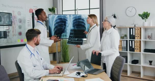 Lékařský koncept, kde sympatická sebevědomí kvalifikovaní multietničtí lékaři pořádají společné setkání na klinice a diskutují o pacientech rentgen hrudníku a plicní sken — Stock video