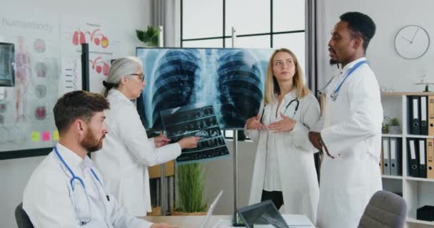 Workflow in kliniek waar aangename succesvolle hoog-geschoolde multiculturele mannelijke en vrouwelijke artsen houden vergadering en bespreken van de resultaten van de borst en longen x-ray, front view — Stockvideo