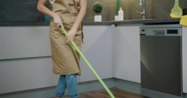 Bayan ev hanımı ahşap zemini ıslak paspasla yıkıyor çıplak ayakla dans ediyor ve müzik dinliyor.