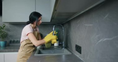 Beyaz, koruyucu sarı eldivenli genç bir kadın mutfak lavabosunu ve musluğu yıkıyor. Ev işleri ve ev idaresi kavramı