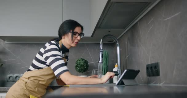 Genç beyaz kadın evdeki mutfakta dijital tablet kullanıyor, rutin.. — Stok video