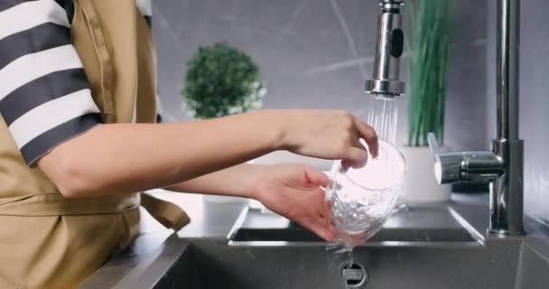 Großaufnahme kaukasischer Frauenhände beim Spülen von Glasgeschirr unter Wasserstrahl in der modernen Wohnküche — Stockvideo