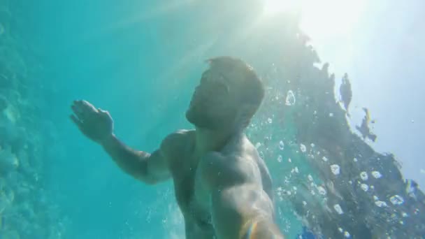 Красивый молодой человек плавает под водой в бирюзовом голубом море теплым солнечным летом — стоковое видео
