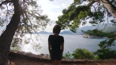 Dişi gezgin, gün batımında inanılmaz deniz manzarasının önünde kollarını açmış kayalıkların tepesine yaklaşıyor.