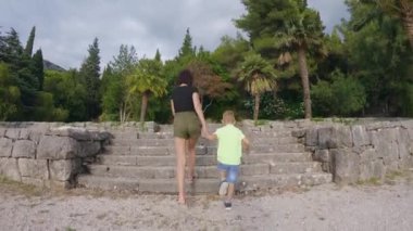 Genç anne ve oğlu yaz günü gün batımında parkta merdivenleri çıkarken eğleniyorlar. Yaşam tarzı. Açık havada.