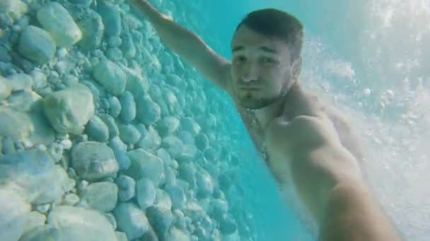 Zpomalený záběr mladého bělocha plavajícího pod vodou v díře se spoustou bublin. Životní styl — Stock video