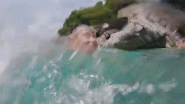 Портрет счастливого улыбающегося мальчика, плавающего в Адриатическом синем море рядом с берегом и смотрящего в камеру — стоковое видео