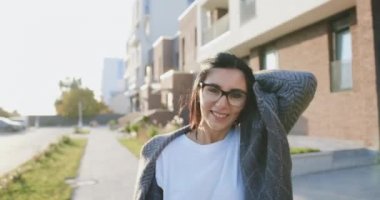 Şehir caddesinde ya da sokakta yürüyen, kameraya poz veren ve güzel bir gülümseme veren neşeli esmer kadının portresi. Rüzgâr saçlarıyla oynuyor. Açık hava, yaşam tarzı.