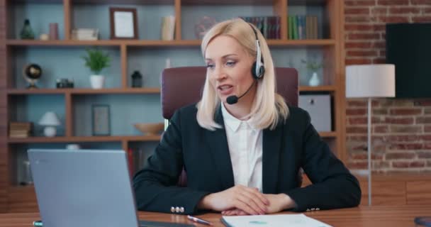 Бізнес жінка середнього віку носить бездротову відеоконференцію з гарнітурою, яка телефонує на ноутбук комп'ютер розмовляти веб-камерою в онлайн-чаті — стокове відео