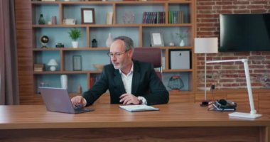 Mature busy business man working at laptop computer and with paper documents analyzing calculation sitting at desk workplace