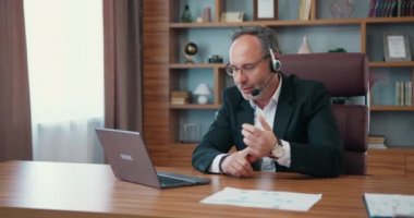 Middle aged business man wearing headset having virtual team meeting on video conference, call using laptop professional training negotiation remote working online in office