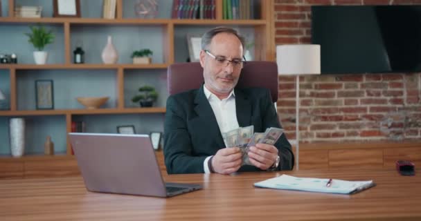 성숙 한 CEO 사업가가 책상에 앉아서 현직 사무실에 현찰을 세고 있습니다. 금융적 독립에 대한 지폐 지불을 확인하는 보스 남성 — 비디오