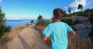 Güneşli bir yaz sabahında plajda koşarken 10-12 yaşlarında mavi tişörtlü bir çocuğun arka görüntüsü. Spor, koşma ve sağlık yaşam tarzı konsepti